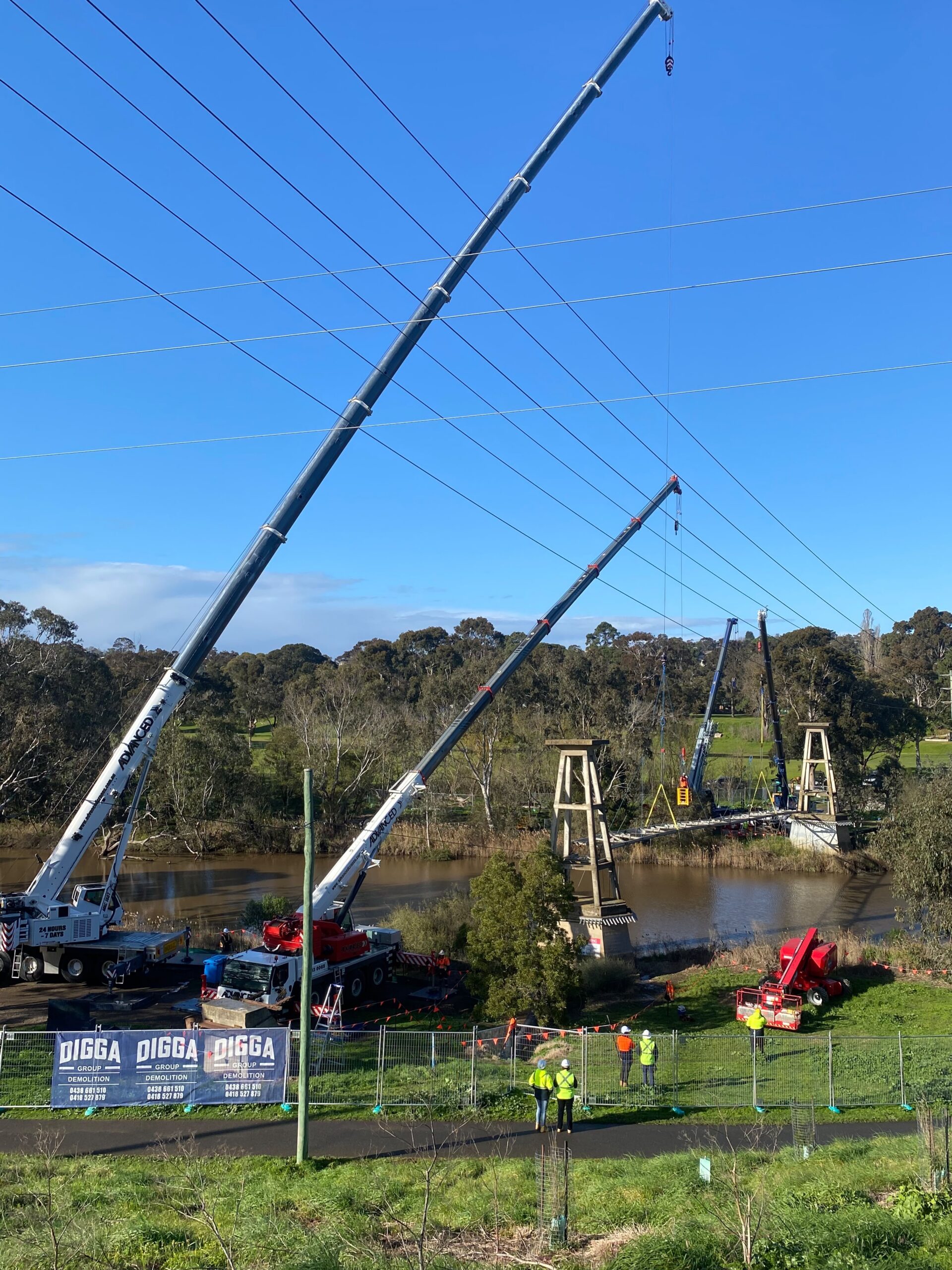 Four cranes working from both banks of the Barwon River to remove the Barwon Water pipe suspension bridge at Fyansford, with Digga Group site fencing and spotters on the shared trail